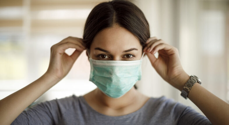 Portrait of young woman putting on a protective mask
