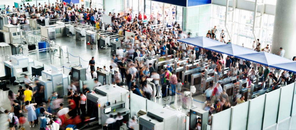 Crowded airport security checkpoint with long lines and dense passenger traffic at screening stations