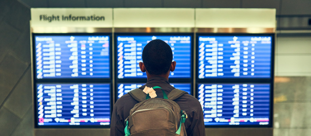 Traveler with a backpack looking at airport flight information display boards to check departure times and gates